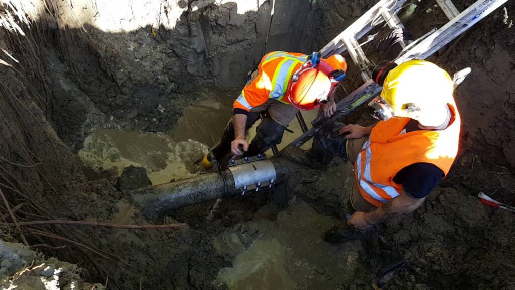 Two workers work in the whole for the water main repair.